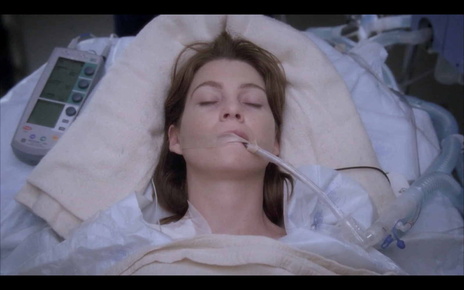 Still from episode 53 of Grey's Anatomy. Meredith Grey lies on a gurney, intubated and surrounded by medical equipment, pale and presumably dead.