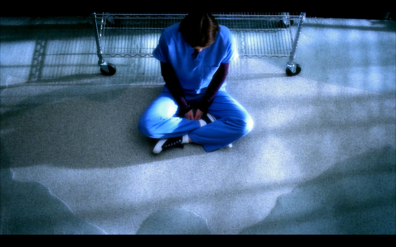 Still from episode 53 of Grey's Anatomy. Meredith Grey is sitting cross-legged in blue scrubs on a hospital floor. Her head is down, and she's surrounded by a growing pool of water.